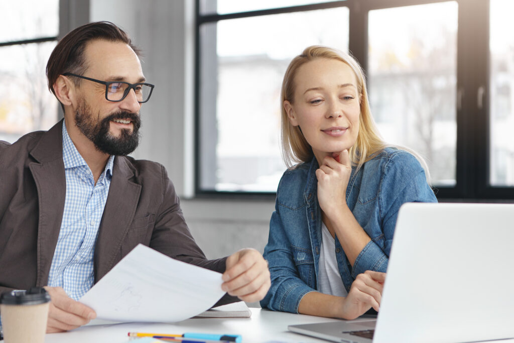 successful mature bearded businessman and his colleague work together in office, discuss statistics. young female shows presentation on laptop computer to her boss, going show it on business meeting